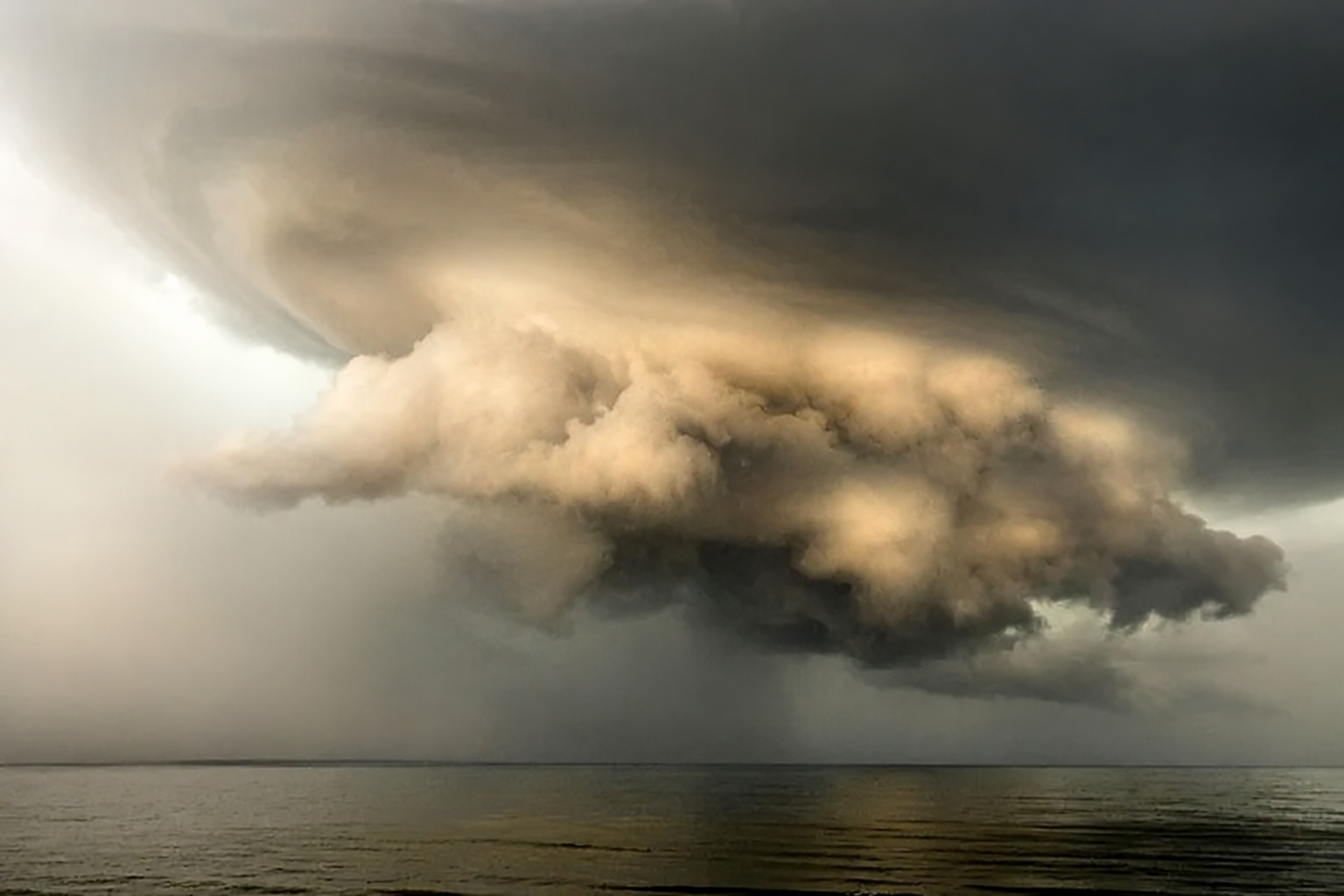 An illuminated storm cloud suspended above open water